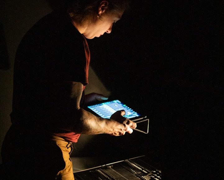 Person nutzt ein Tablet zur Steuerung einer technischen Anlage oder eines Systems in einer dunklen Umgebung.