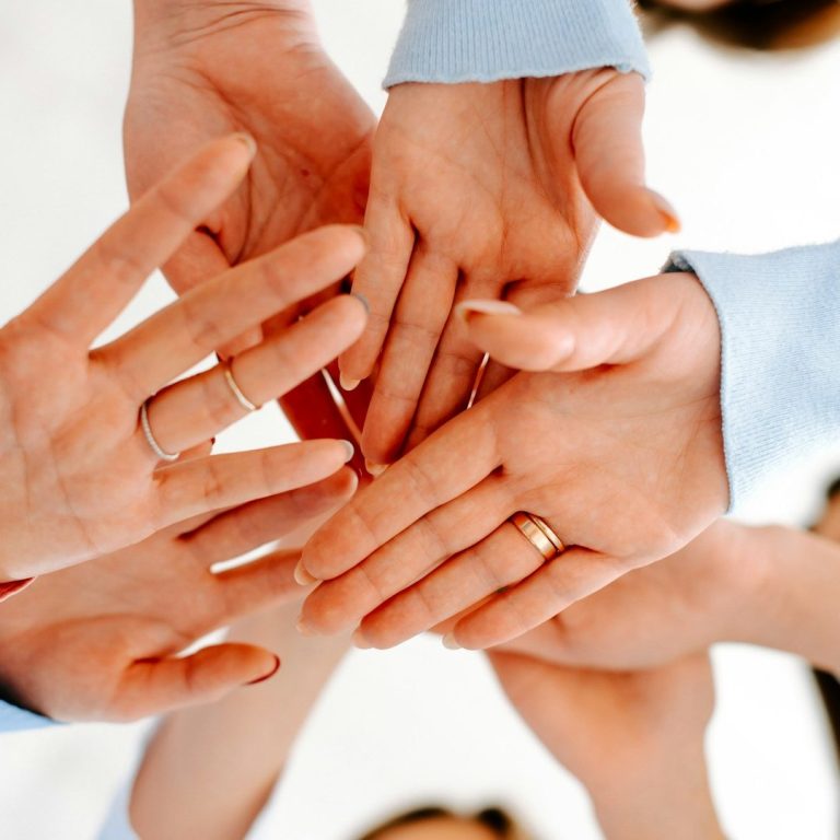 Mehrere Personen legen ihre Hände übereinander, als Zeichen für Teamarbeit, Vertrauen und gemeinsames Arbeiten.